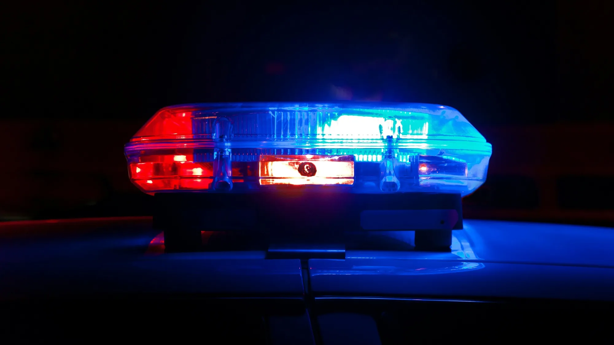 Close-up of a red and blue police light bar on the roof of a patrol car at night