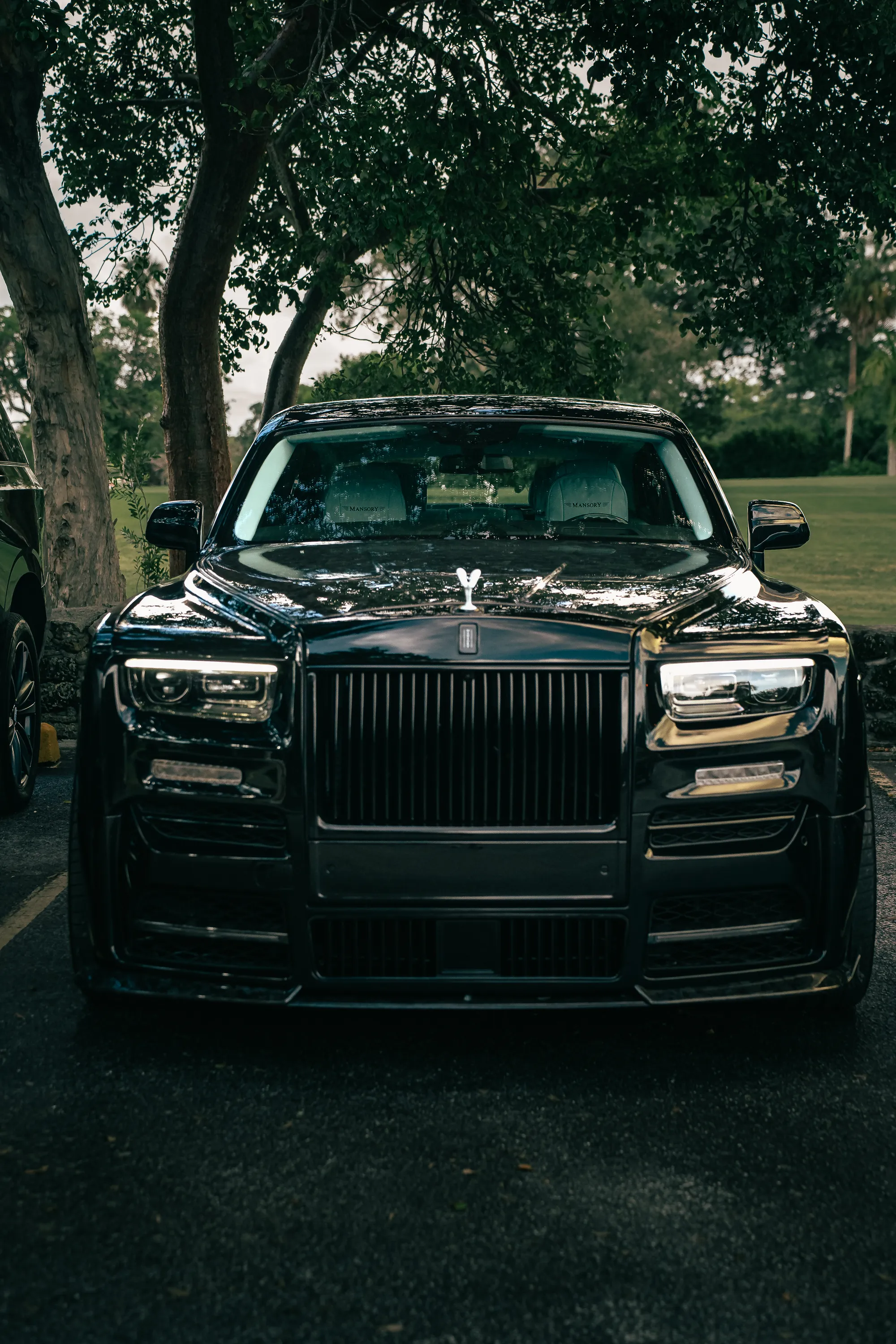 Black Rolls-Royce Phantom 2026 by MANSORY from the Prestige Guard fleet, front view under trees